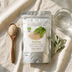 one wooden teaspoon heaped with medium-coarse pale beige psyllium husk granules, one clear glass of water 250ml, silver stand-up pouch product bag beside it
