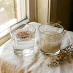 Two glass tumblers side by side , left glass contains clear water with one teaspoon of medium-coarse psyllium husk grains just added, grains visible on water surface, right glass shows thick translucent gel formed after 5 minutes